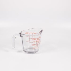 A clear glass measuring cup with red markings on a white background, perfect for culinary use.